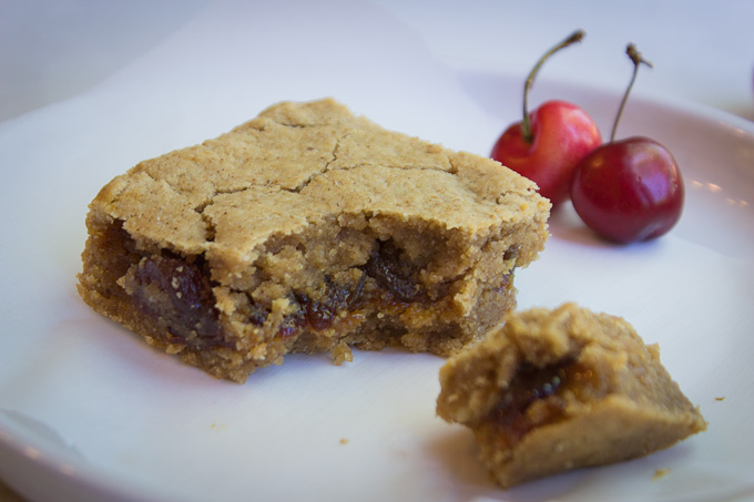 Cherry Jubilee Blondies with a bite taken out of the corner showing the jam on the inside, with a white background and fresh cherries around it