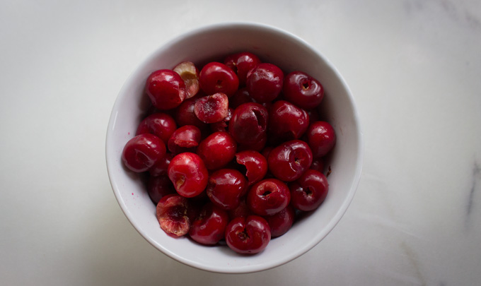 Overhead view of a white bowl filled with fresh sweet cherries on a white board