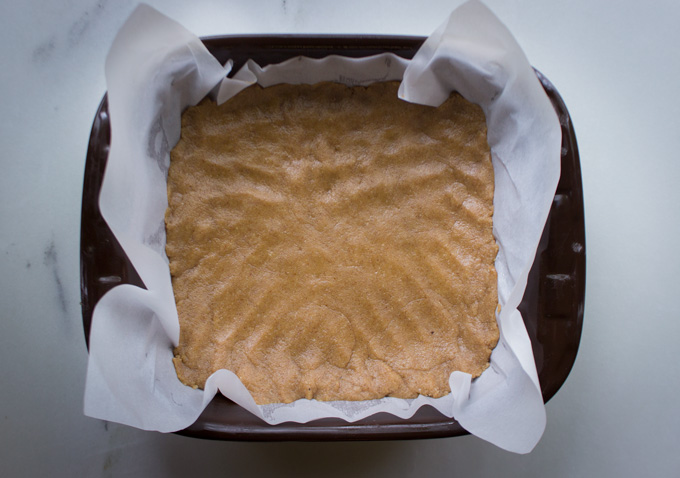 Overhead view of shortbread dough pressed into a brown baking dish filled with parchment paper