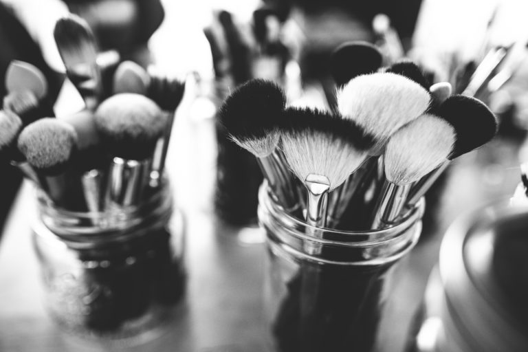 Black and white image of various makeup brushes and tools in glass jars