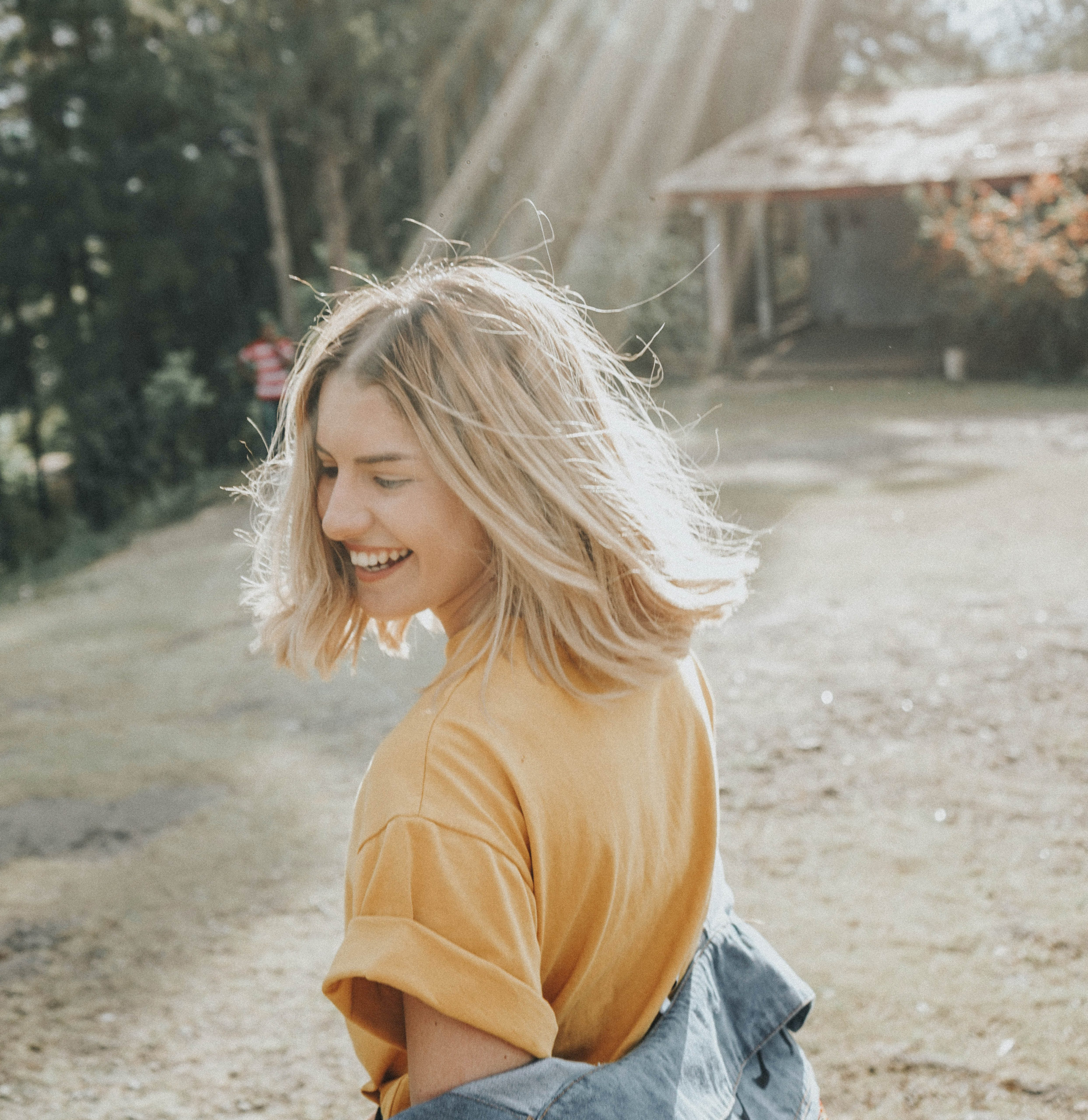 Smiling Woman in tee and jean jacket with tree and sun rays in background